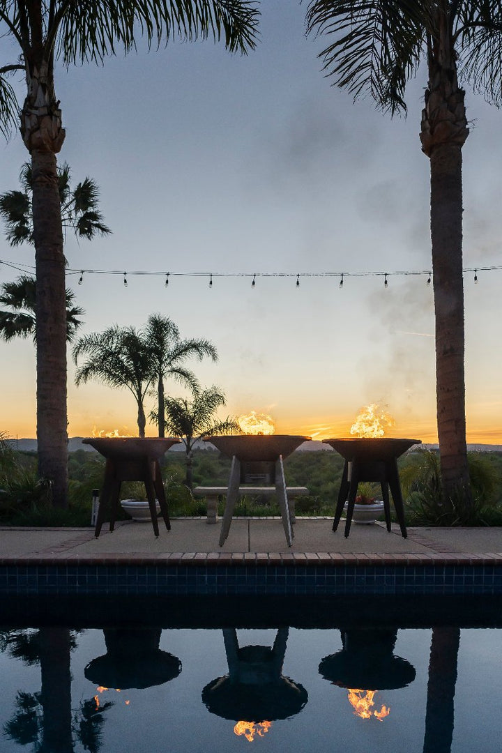 3 Mojave Grills - powder coated black, stainless steel and corten steel flaming under the palm trees by the swimming pool.