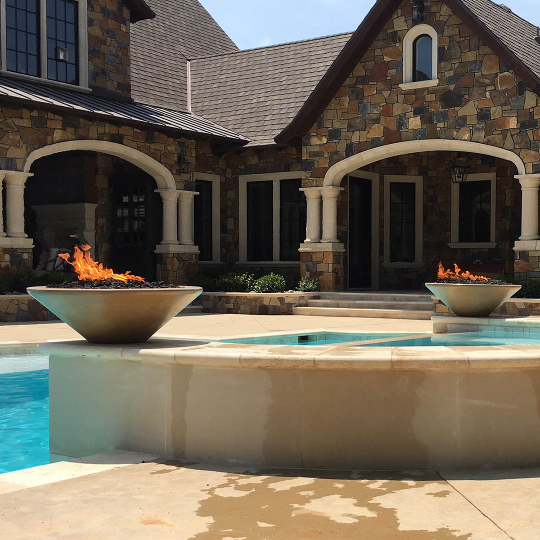 Two Cazo fire bowls beside a pool in front of a beautiful home.